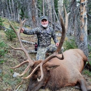 Hunter proudly showcasing a trophy bull elk harvested during a guided hunt in Wyoming’s rugged wilderness.